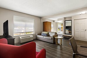 A modern living room with a sofa, red armchair, and a television on a desk. - Country Inn & Suites by Radisson, Hinesville, GA (Hinesville)
