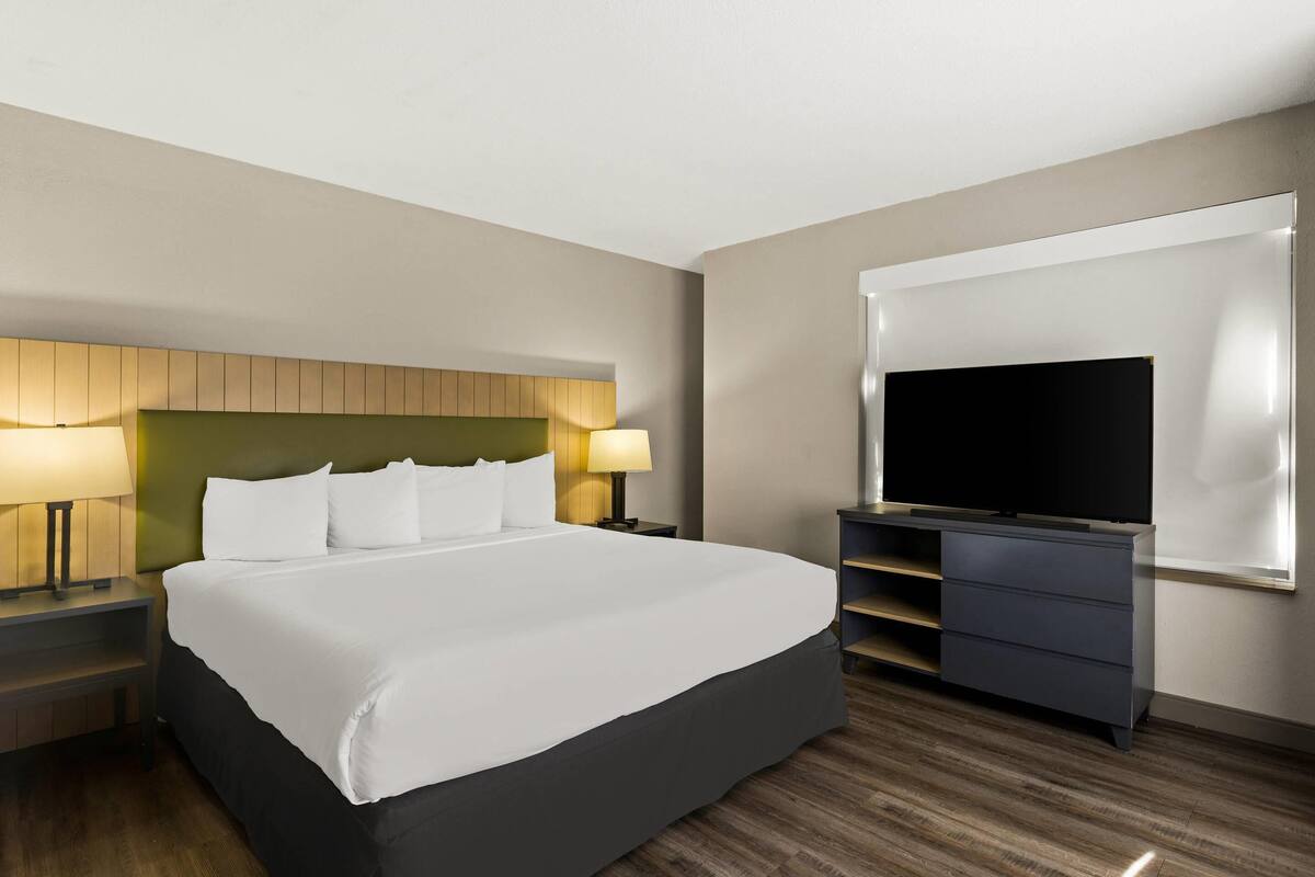 A hotel room with a large bed, two bedside tables with lamps, a flat-screen TV, and a dresser.
