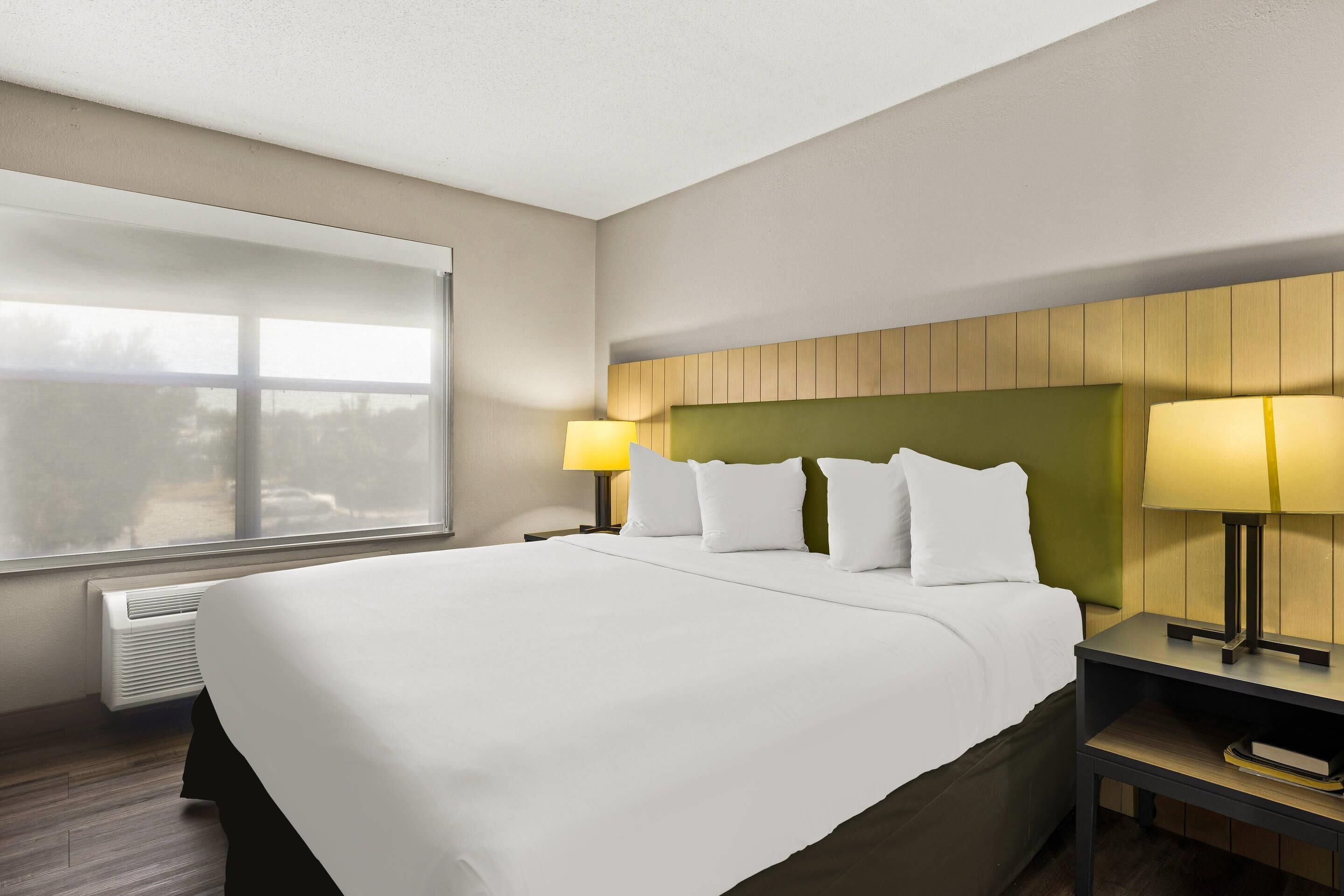 Habitación de hotel con una cama grande, dos mesitas de noche con lámparas, una ventana con persianas y un calentador de pared.