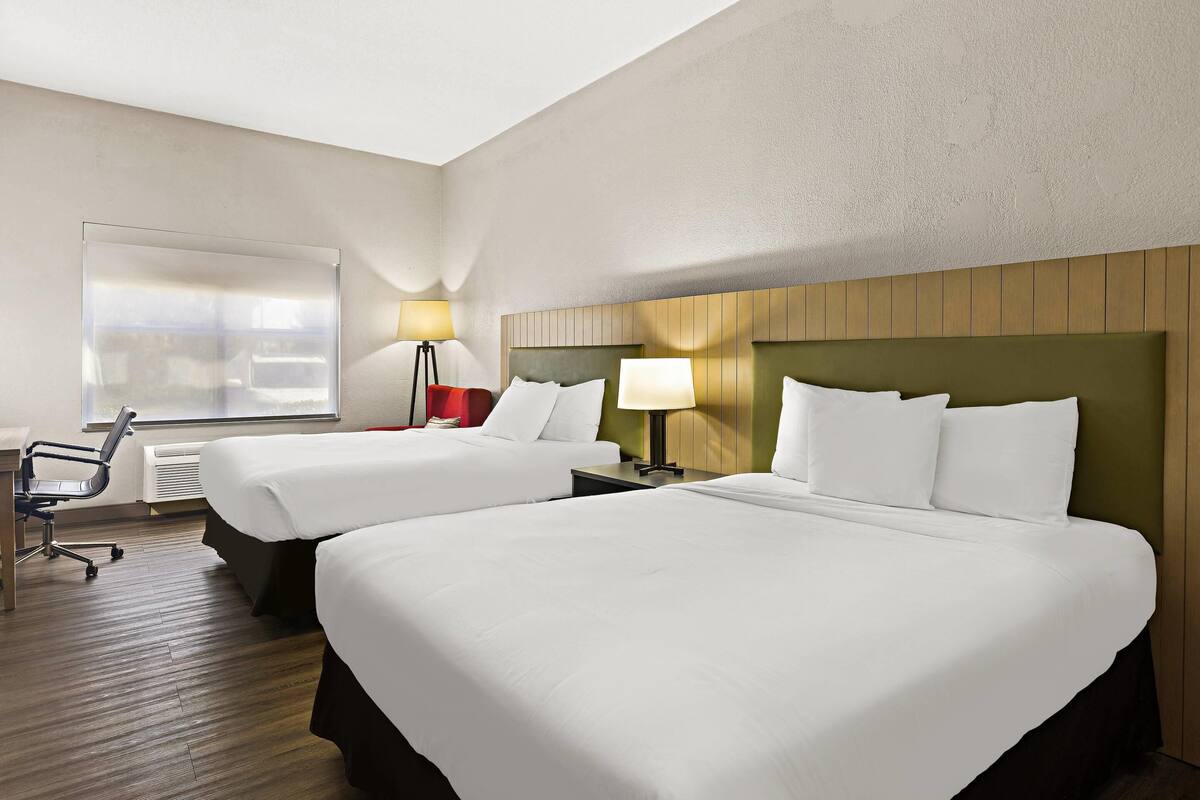A hotel room with two beds, a desk, a chair, and a window.