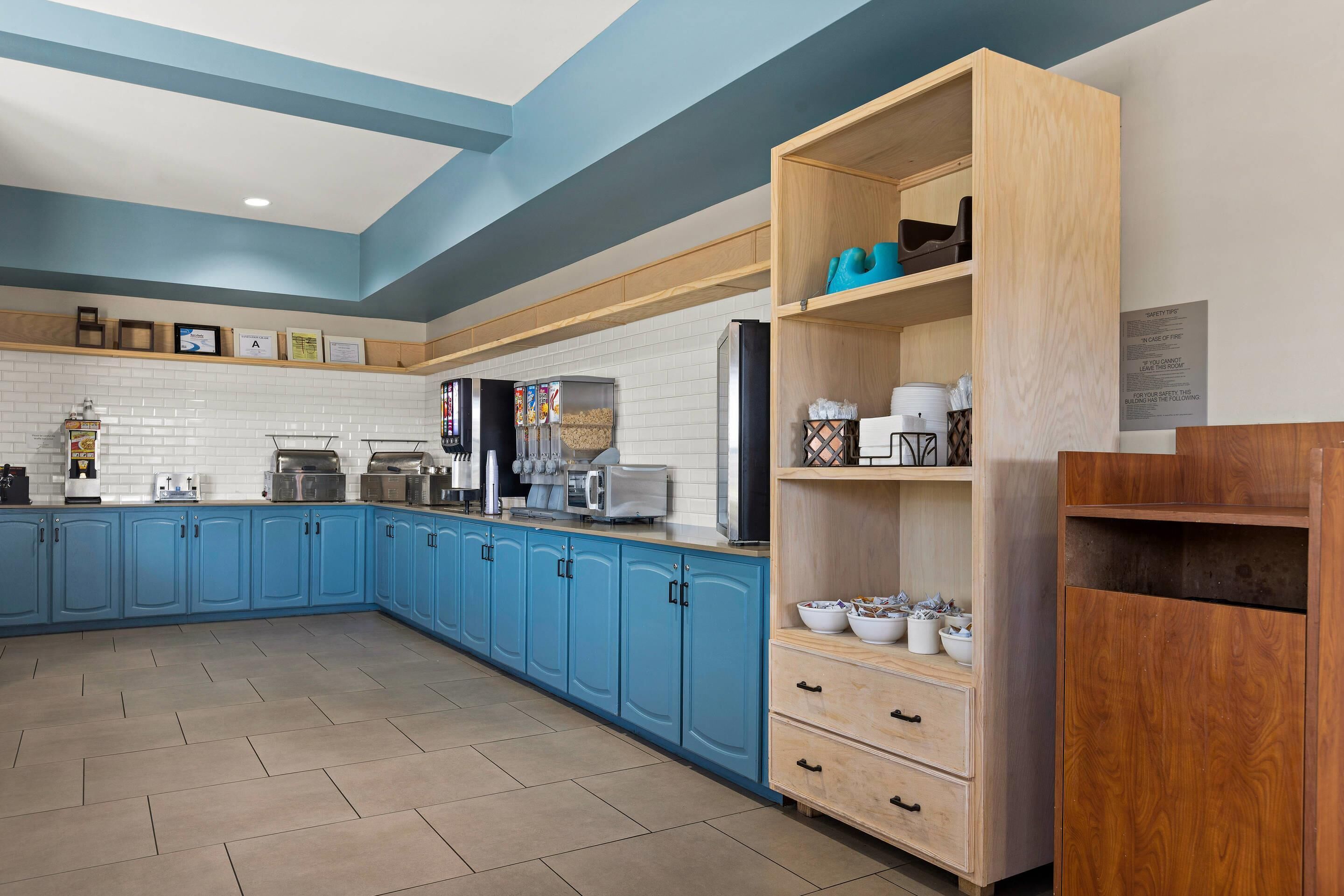 A modern kitchen with blue cabinets, a wooden pantry, and various appliances.