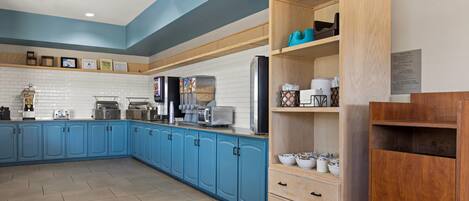 A modern kitchen with blue cabinets, a wooden pantry, and various appliances.