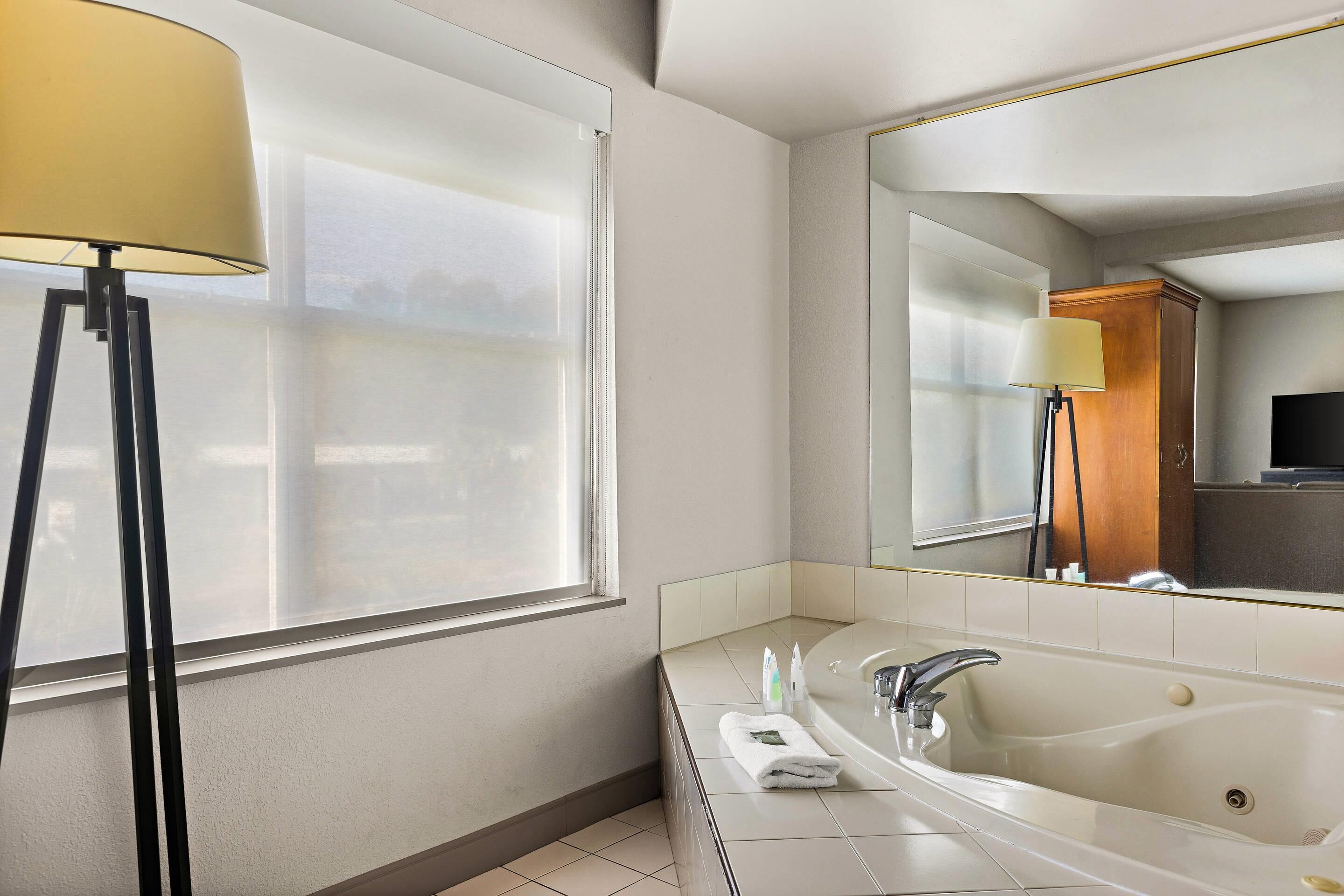 A modern bathroom with a large mirror, a bathtub, a sink, and a floor lamp.