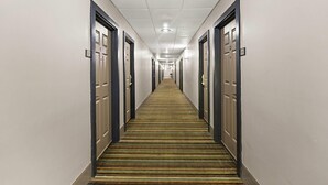 Un long couloir étroit, typique des hôtels, avec des portes de chaque côté, une moquette à motifs et un plafond doté d’un éclairage encastré.