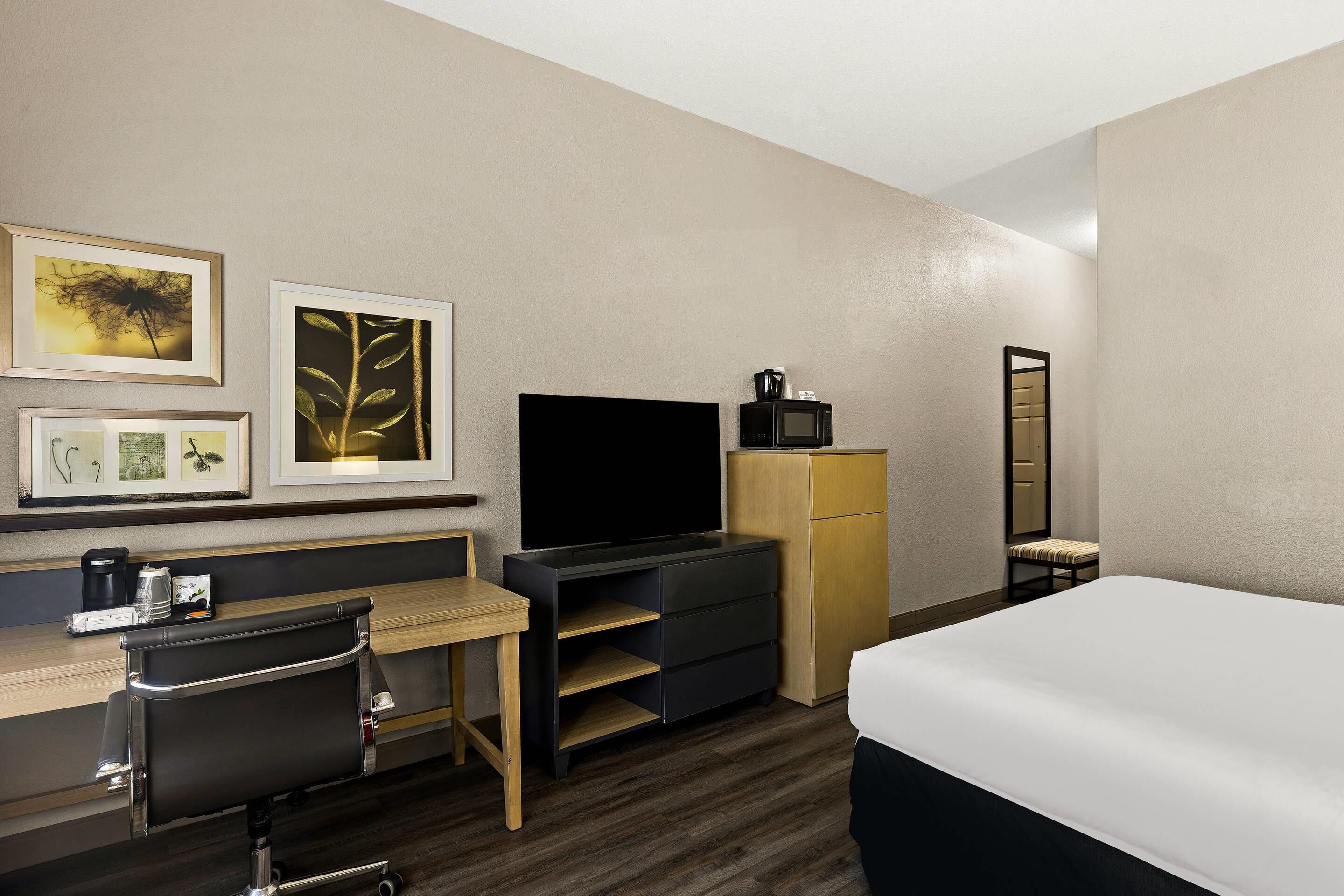 Una habitación de hotel con cama, escritorio, silla, televisor y armario.
