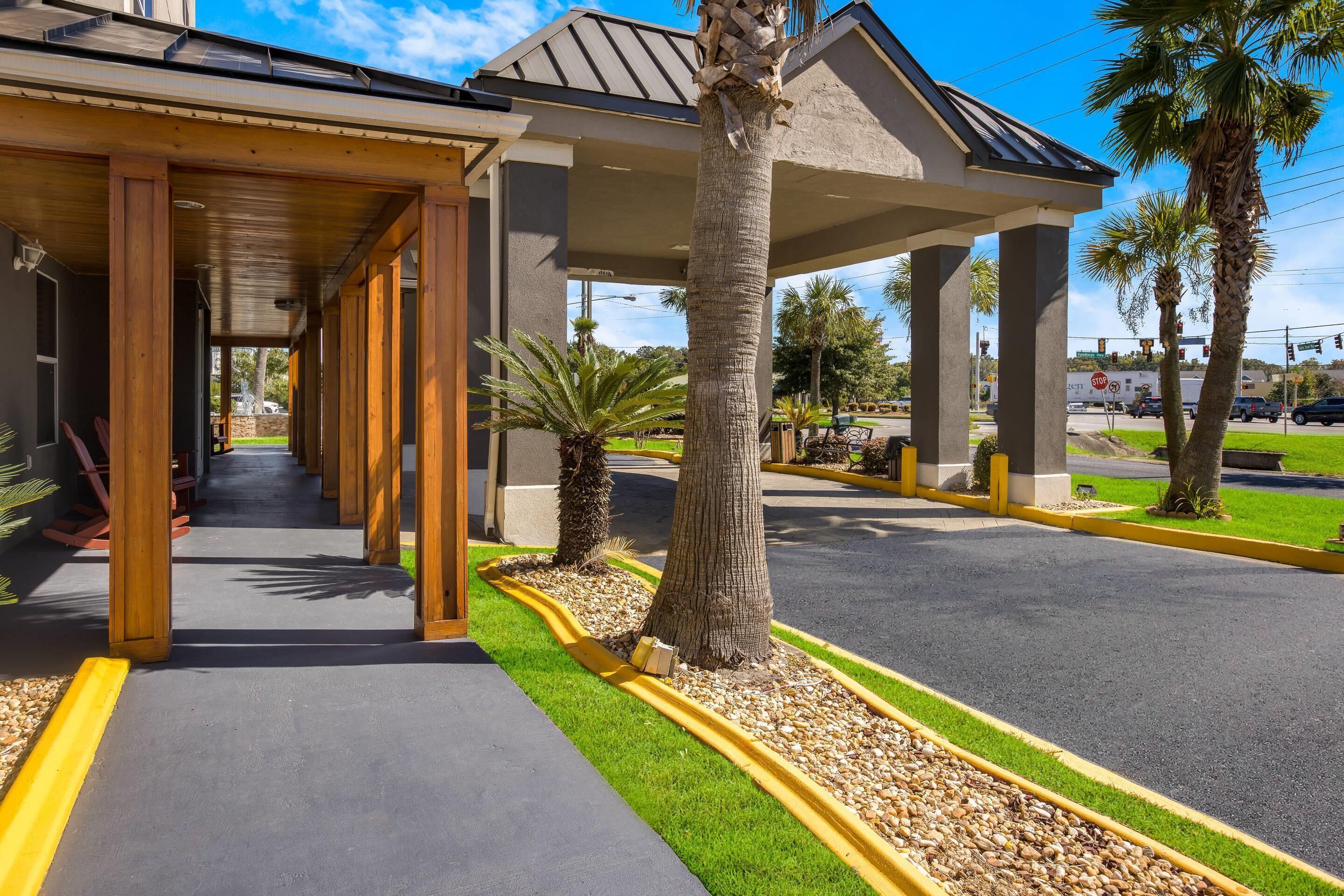 A covered walkway with wooden columns, palm trees, and a parking lot.