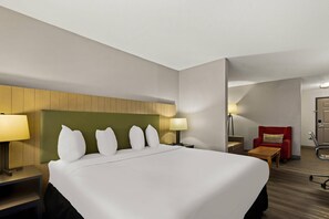 A hotel room with a large bed, bedside lamps, a desk, a chair, and a red armchair.