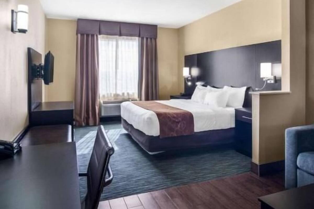 Une chambre d’hôtel avec un lit, un bureau, une chaise, une télévision et une fenêtre avec des rideaux.