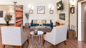A modern lobby with a blue sofa, two patterned armchairs, a coffee table, and a fireplace. - Comfort Suites Odessa near University (Odessa)