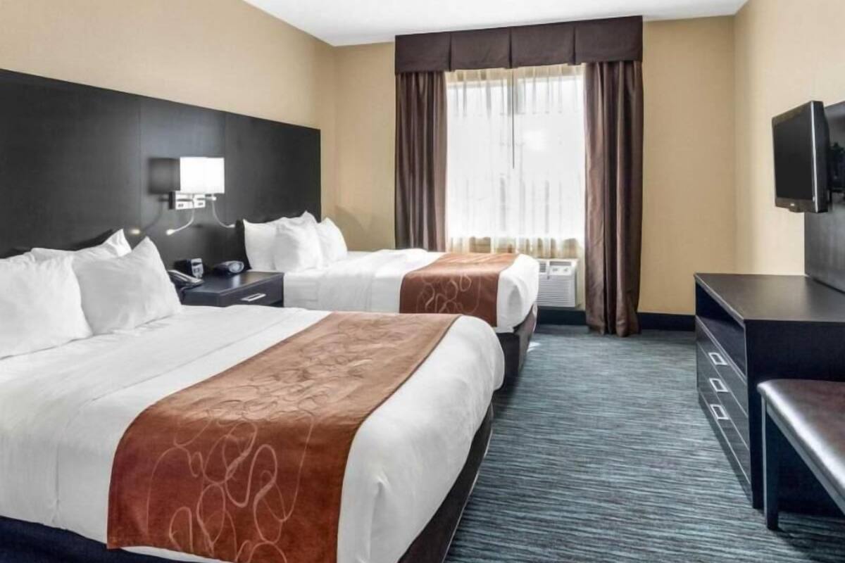 Une chambre d’hôtel avec deux lits, un bureau, une télévision et une fenêtre avec des rideaux.