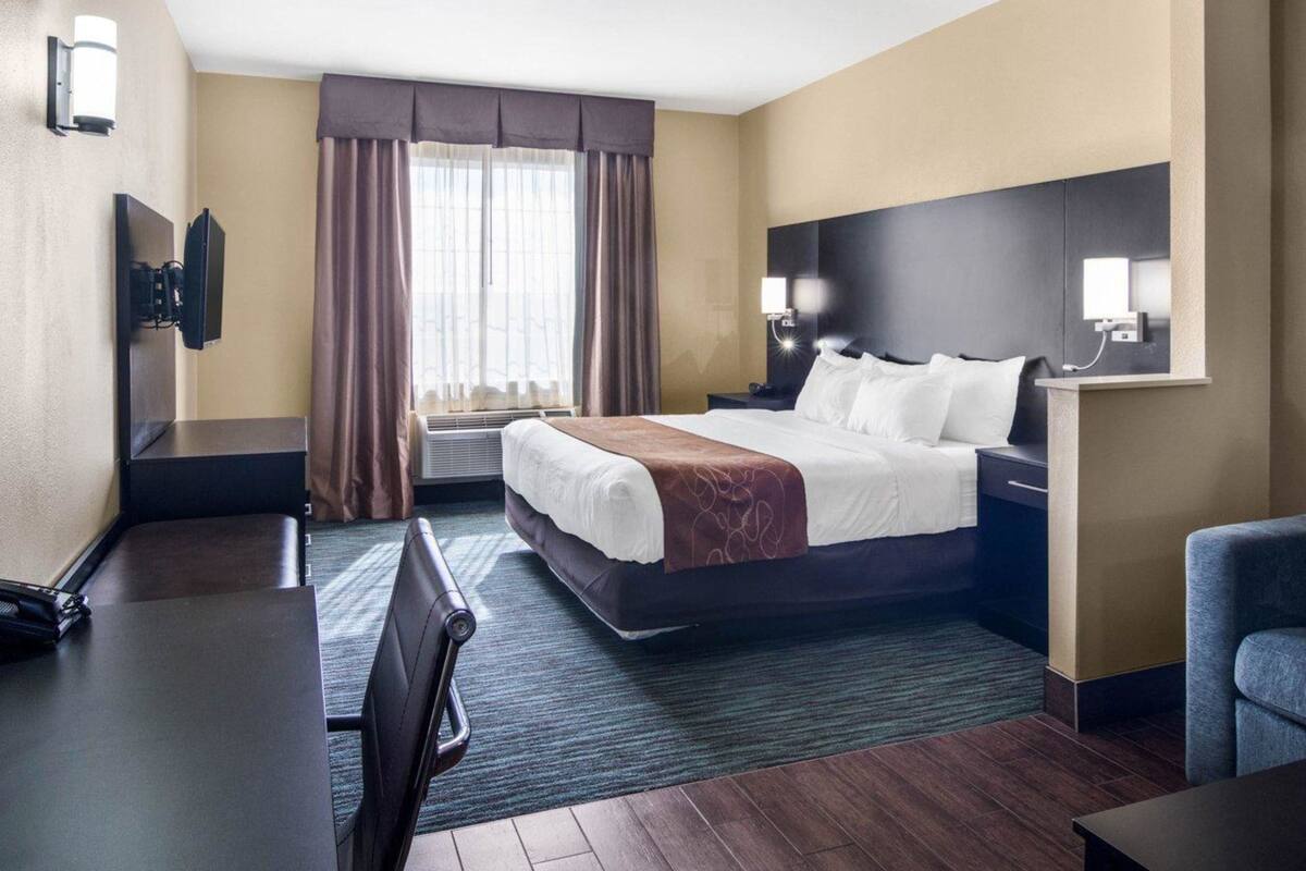 Une chambre d’hôtel équipée d’un lit, d’un bureau, d’une chaise et d’un téléviseur fixé au mur.