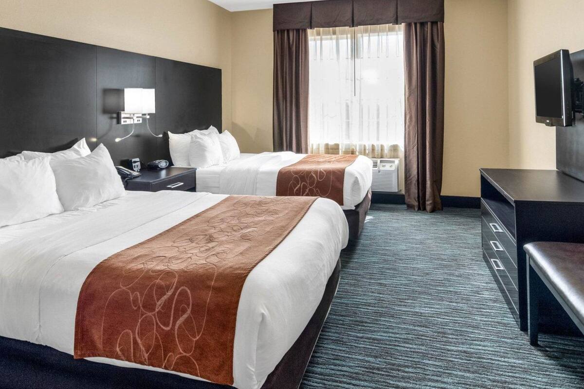 Une chambre d’hôtel avec deux lits, un bureau, une télévision et une fenêtre avec des rideaux.