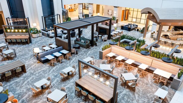 Un vaste patio intérieur, doté de plusieurs espaces de détente, notamment des tables et des bancs, et agrémenté de plantes et d’une architecture moderne.