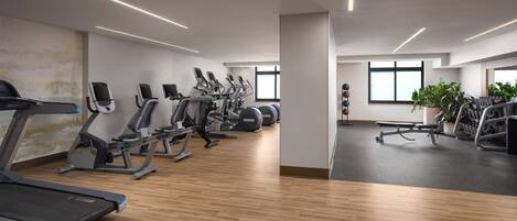 Ein Fitnessraum mit verschiedenen Trainingsgeräten, Holzböden und großen Fenstern.