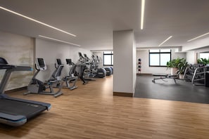Un gimnasio con diverso equipo de ejercicio, suelo de madera y ventanas amplias.