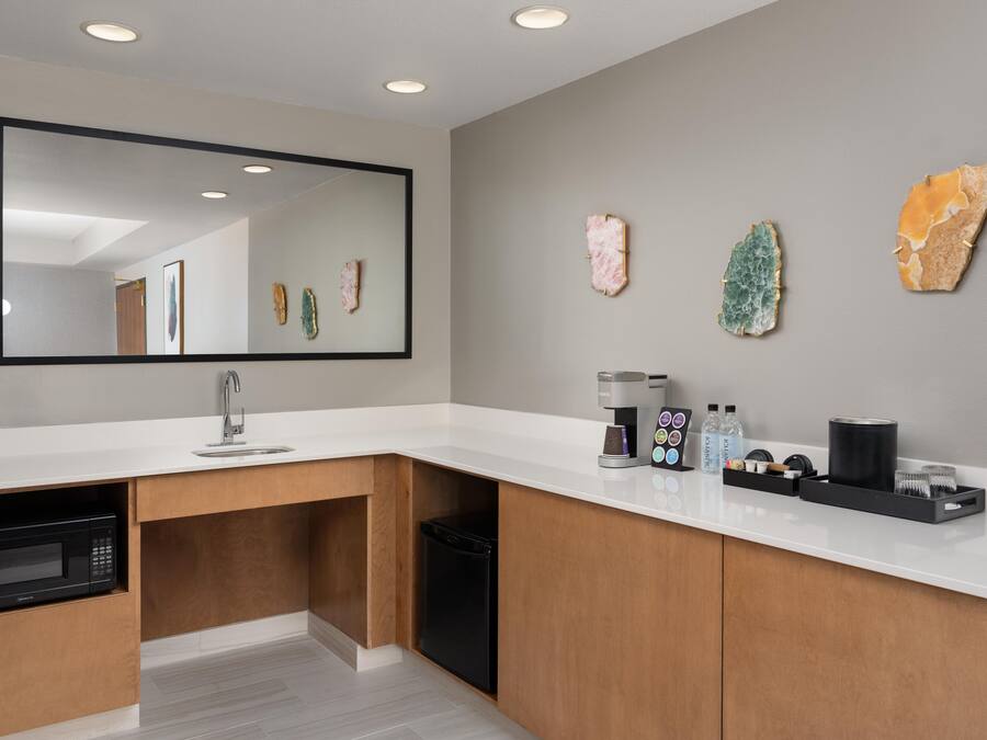 Een moderne badkamer met een wit aanrecht, een wastafel, een koffiezetapparaat en decoratieve stenen aan de muur.