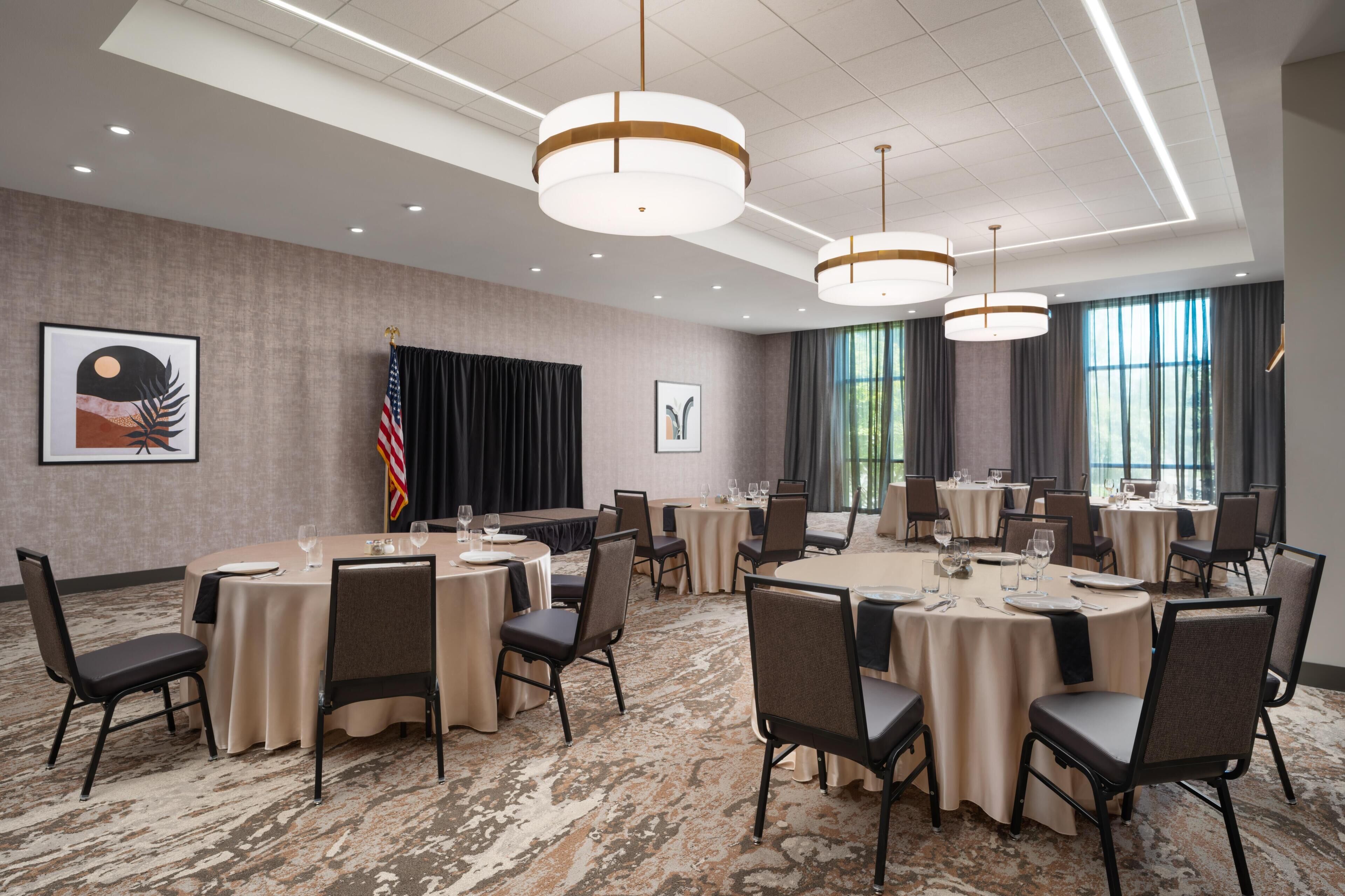A conference room with round tables, chairs, and a stage with curtains.