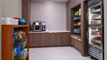 A self-service kiosk area with a coffee machine, a beverage dispenser, and a refrigerated section stocked with snacks and drinks.
