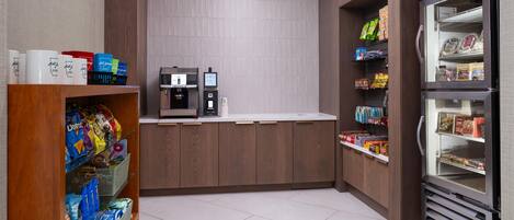 A self-service kiosk area with a coffee machine, a beverage dispenser, and a refrigerated section stocked with snacks and drinks.
