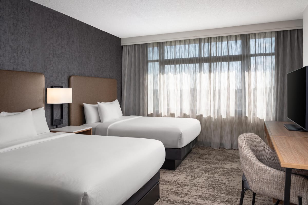 Ein Hotelzimmer mit zwei Betten, einem Schreibtisch, einem Sessel und einem Fernseher.