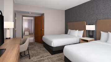 A hotel room with two beds, a desk, a chair, a TV, and a bathroom visible through an open door.
