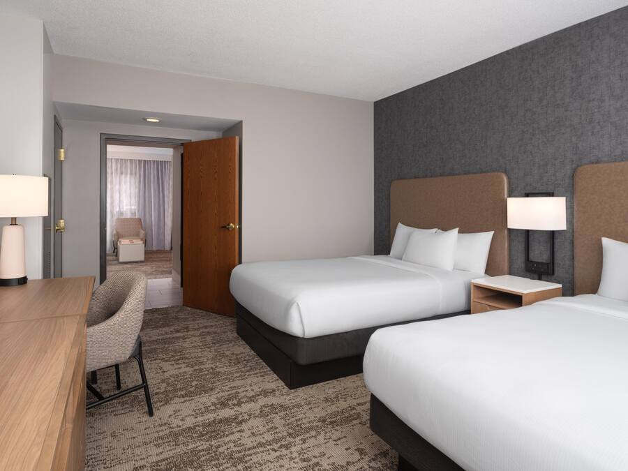 A hotel room with two beds, a desk, a chair, a TV, and a bathroom visible through an open door.