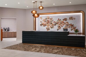 Una reception hotel dal design moderno, un'opera d'arte a parete e una macchina per caffè sullo sfondo.