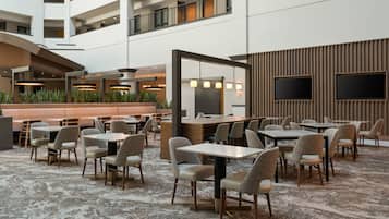 A hotel lobby with multiple dining areas, a reception desk, and a large TV screen.