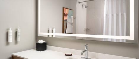 A modern bathroom with a large mirror, a white sink, and a shower curtain.
