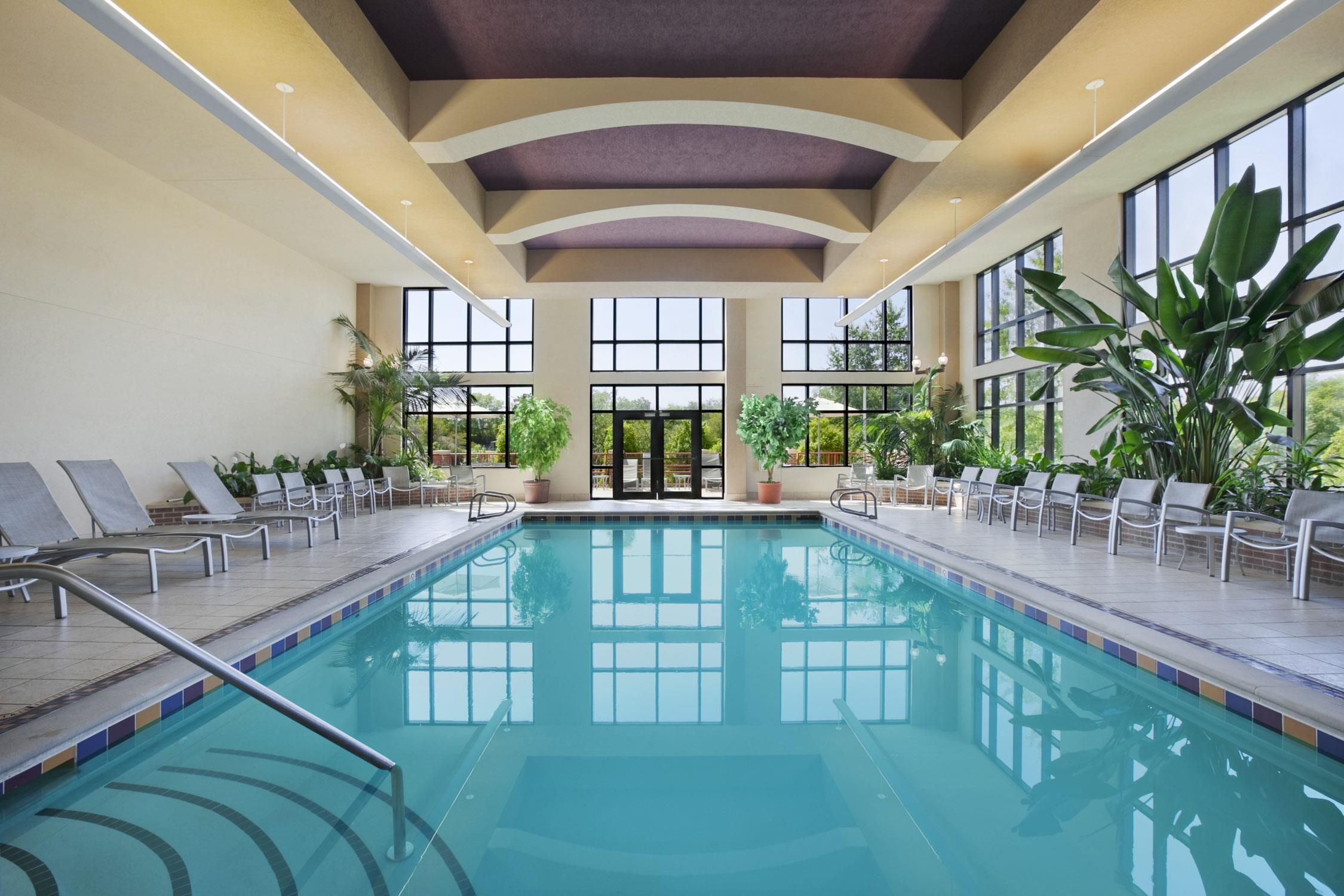 An indoor swimming pool with lounge chairs and potted plants.