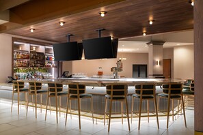 A modern bar area with a long counter, multiple bar stools, and a television mounted above the bar.