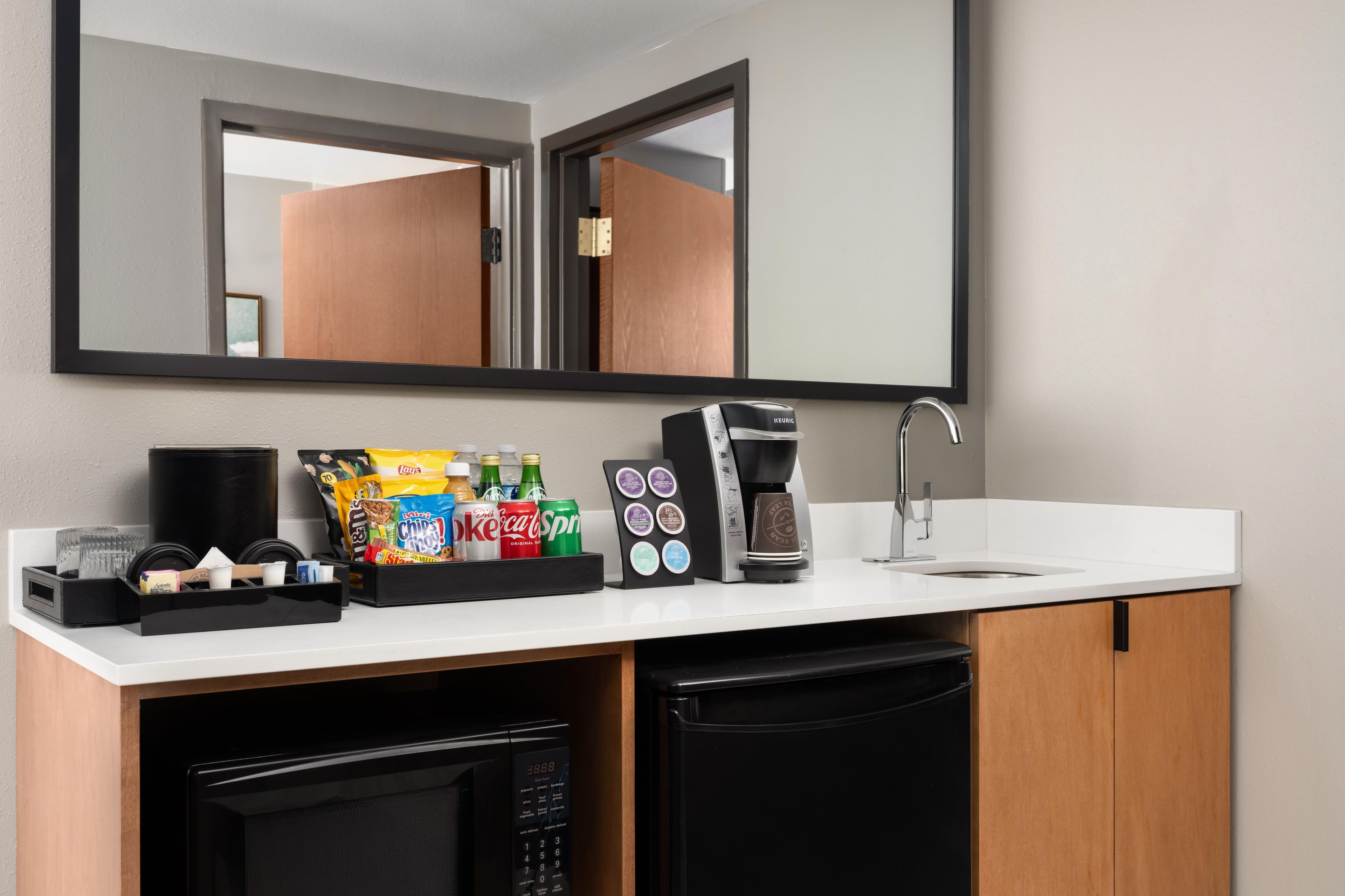 A kitchenette with a coffee maker, a microwave, a sink, and a mirror above the counter.