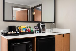 A kitchenette with a coffee maker, a microwave, a sink, and a mirror above the counter.
