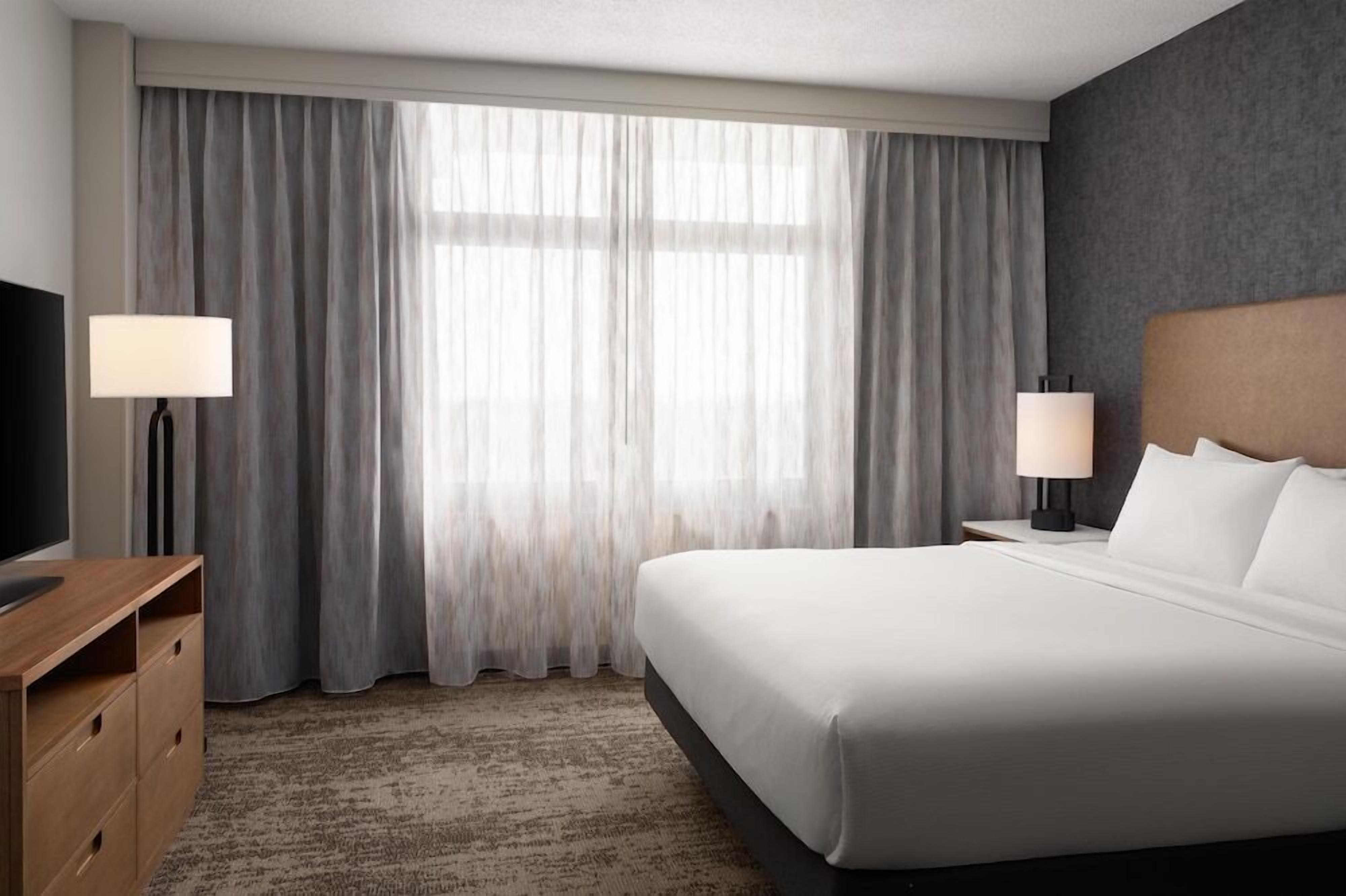 Ein Hotelzimmer mit einem großen Bett, zwei Nachttischlampen, einem Fernseher und einem Schreibtisch.