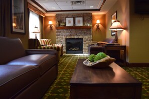 A hotel room with a fireplace, leather sofa, armchairs, a coffee table with a decorative bowl, and two wall-mounted lamps. - Holiday Inn Express Hocking Hills-Logan by IHG (Logan)