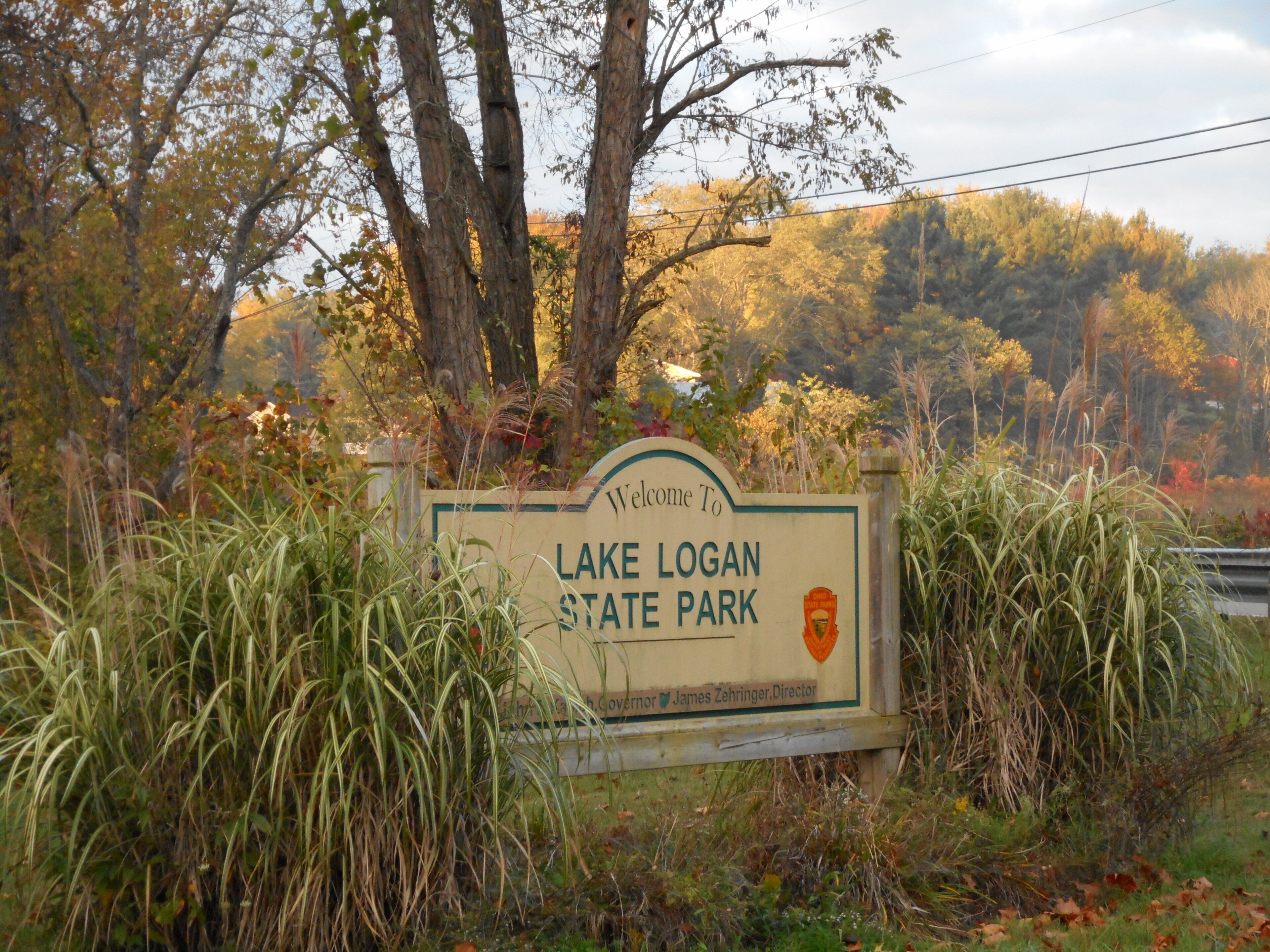 A welcome sign for Lake Logan State Park with a natural backdrop of trees and grass.