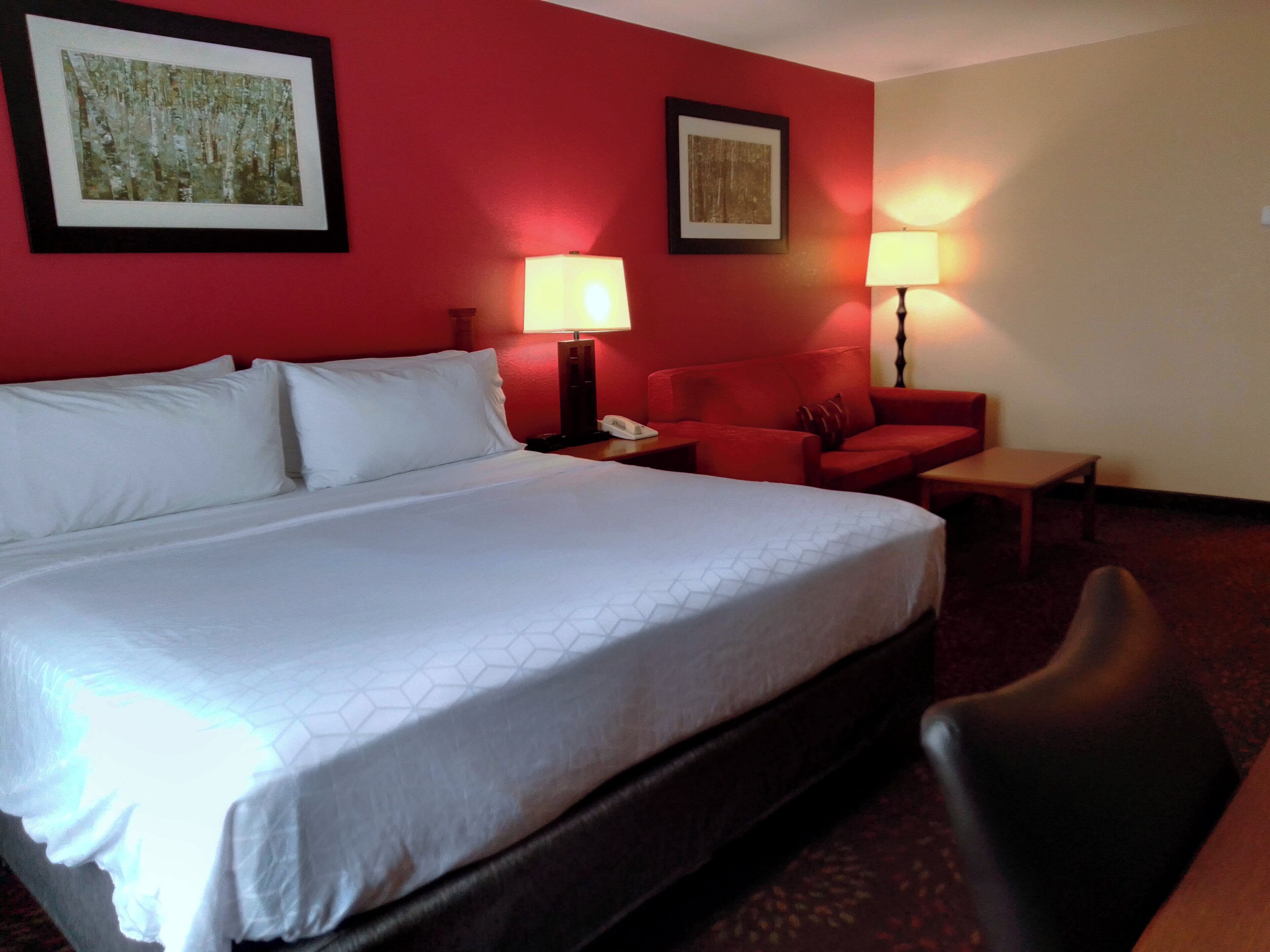 A hotel room with a large bed, two red armchairs, a small table, and two wall-mounted lamps.