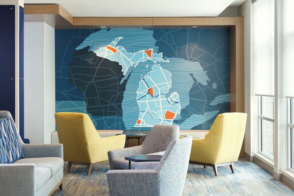 Una hall d'albergo moderna con un grande murale astratto raffigurante una mappa, posti a sedere confortevoli e vista sull'esterno.