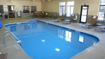 Piscina interna com água cristalina, cercada por espreguiçadeiras e uma parede de pedra.