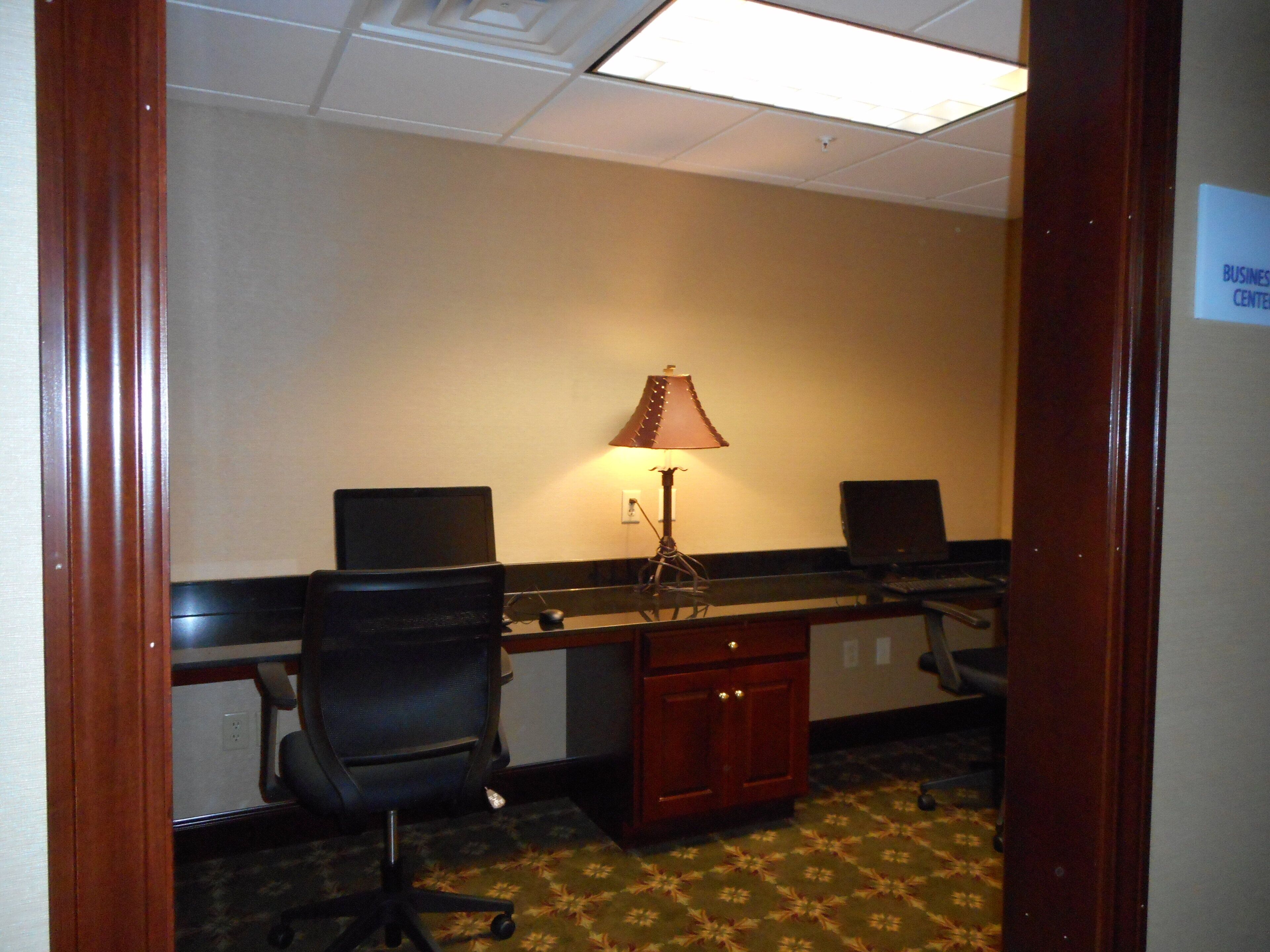 A room with two black office chairs, a desk with a lamp, and a small cabinet.