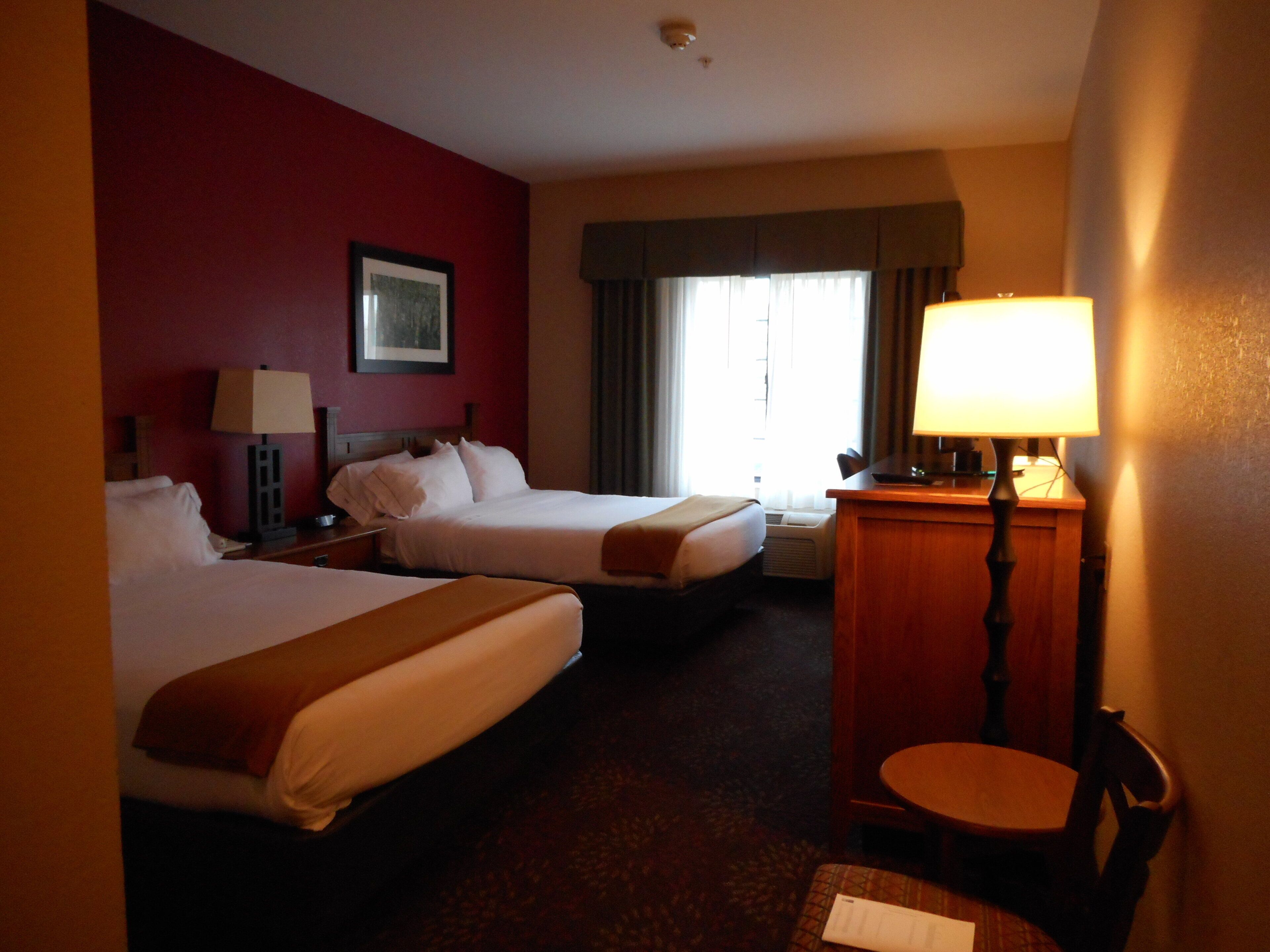 Ein Hotelzimmer mit zwei Betten, einem Schreibtisch, einem Stuhl und einem Fenster mit Vorhängen.