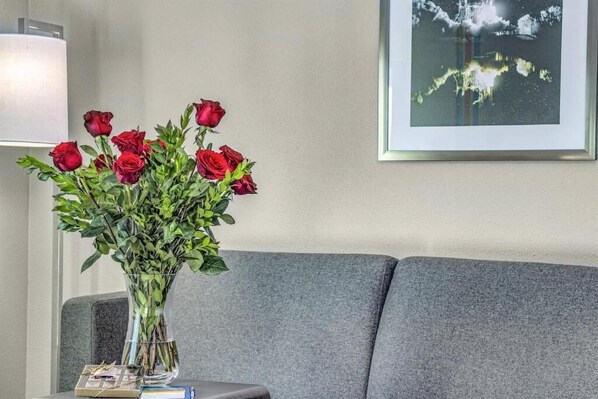 Un jarrón con rosas rojas sobre una mesa junto a un sofá gris.