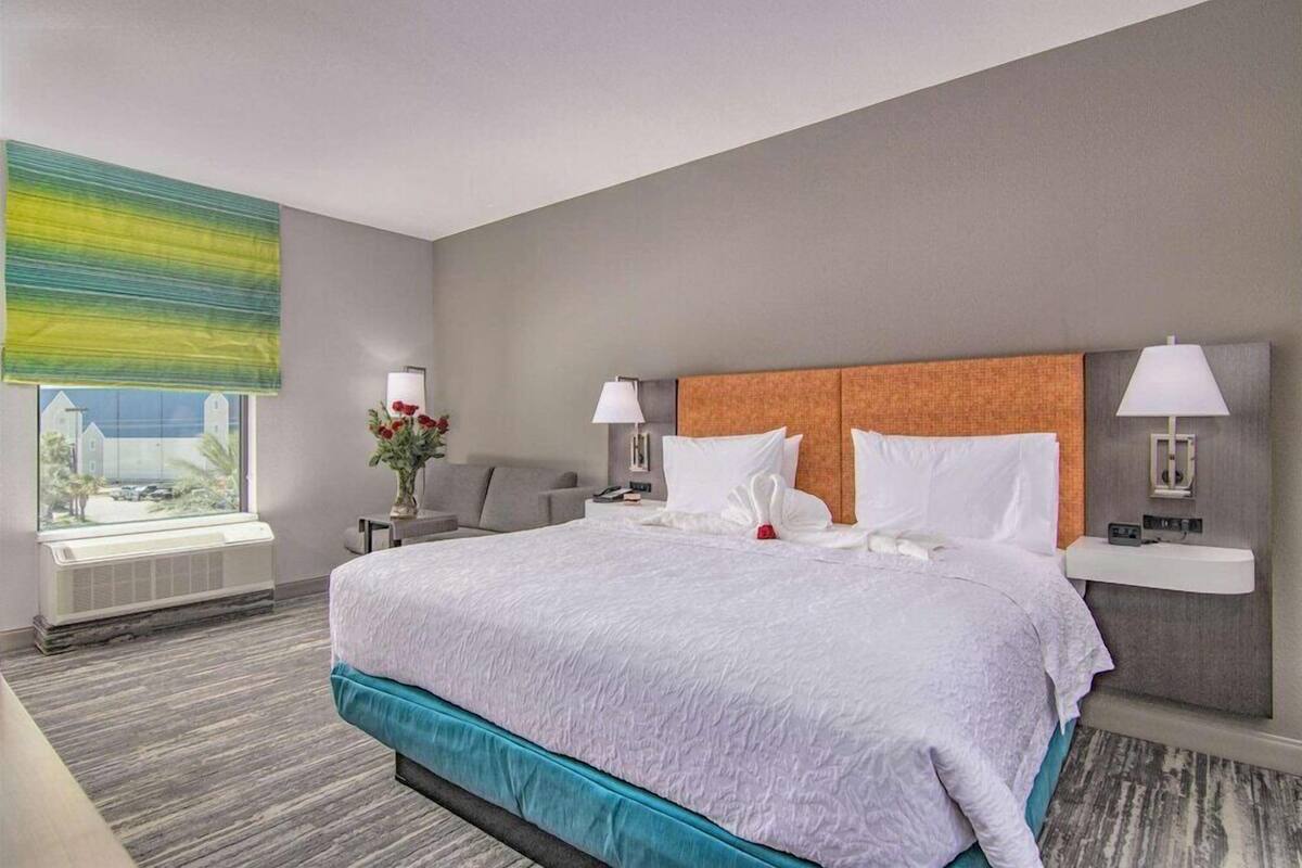A hotel room with a large bed, two bedside tables with lamps, a window with a view, and a radiator.
