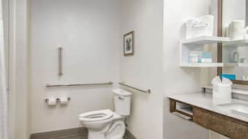 Un baño con inodoro, ducha, barra de apoyo, toallero y tocador con espejo.