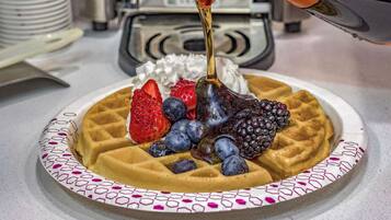 Een wafel met aardbeien, bosbessen, bramen en slagroom, waarover siroop wordt gegoten.