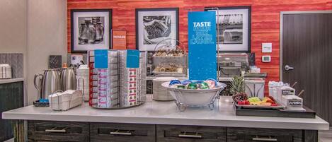 A hotel reception area with a counter displaying various amenities like coffee makers, snack boxes, and a fruit tray.