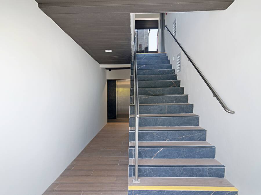A modern staircase with marble steps and a metal handrail, leading to an elevator.