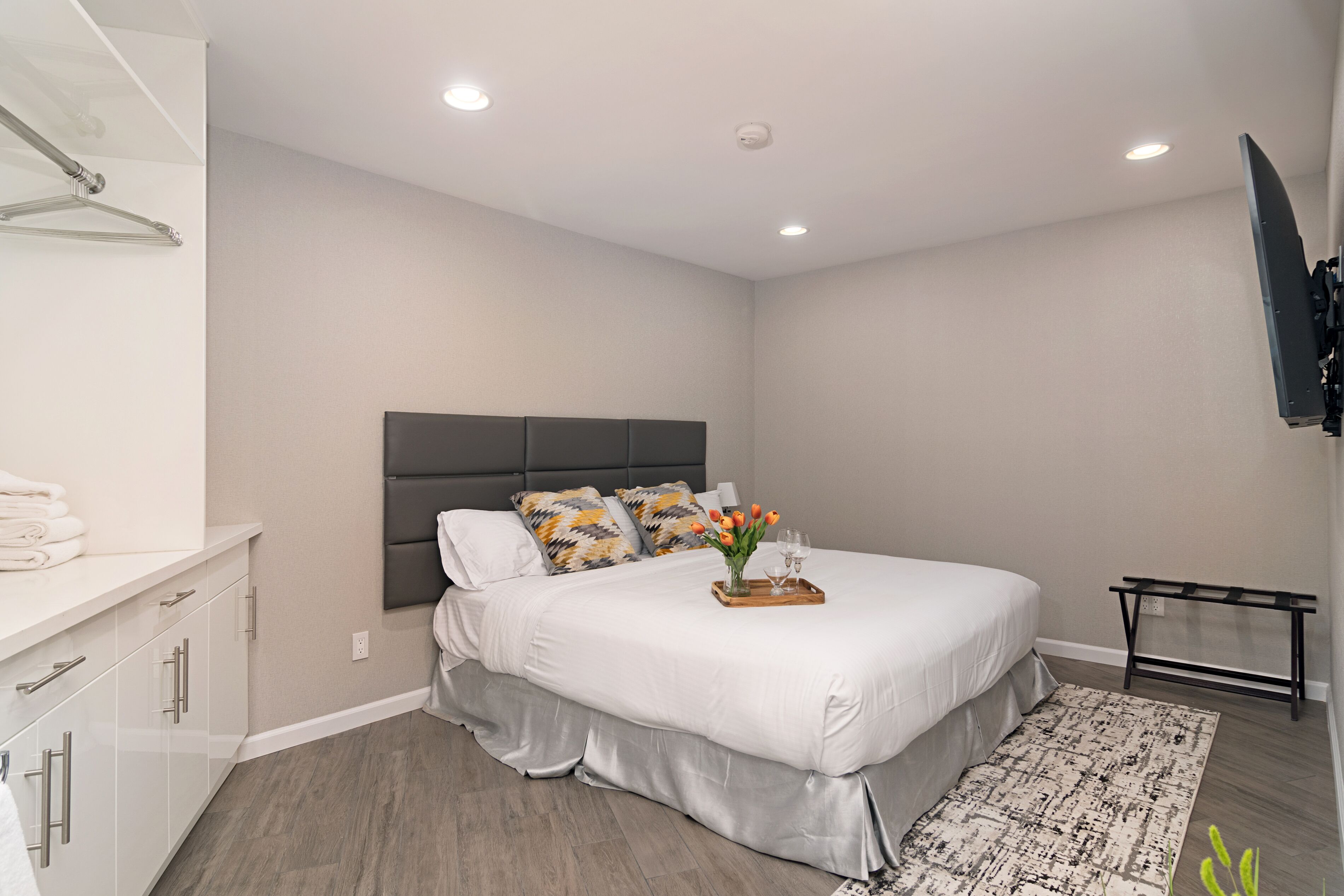 Une chambre moderne avec un grand lit, une table de chevet sur laquelle est posé un plateau de fleurs et un téléviseur fixé au mur.