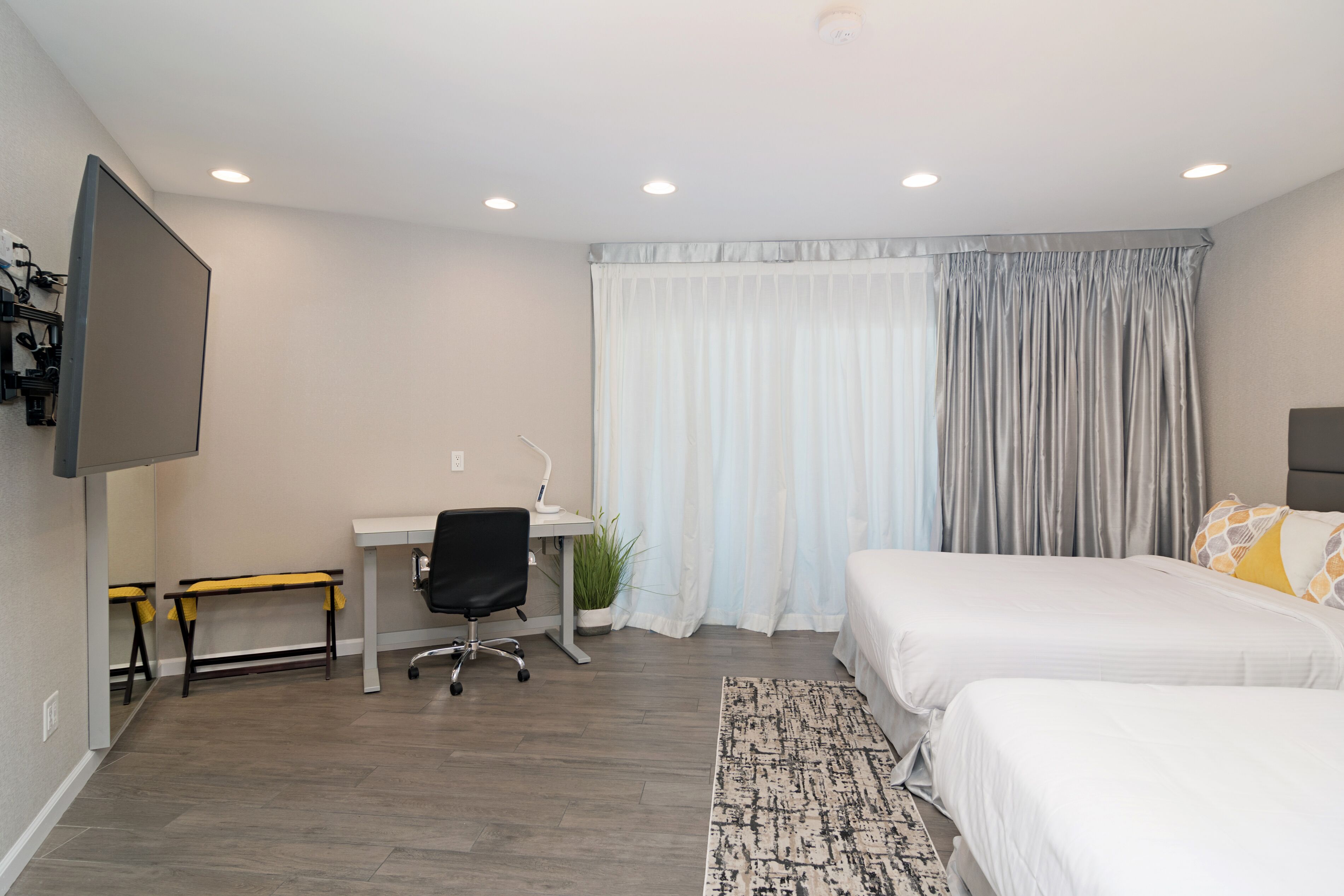 A hotel room with two beds, a desk with a chair, a TV mounted on the wall, and a window with curtains.