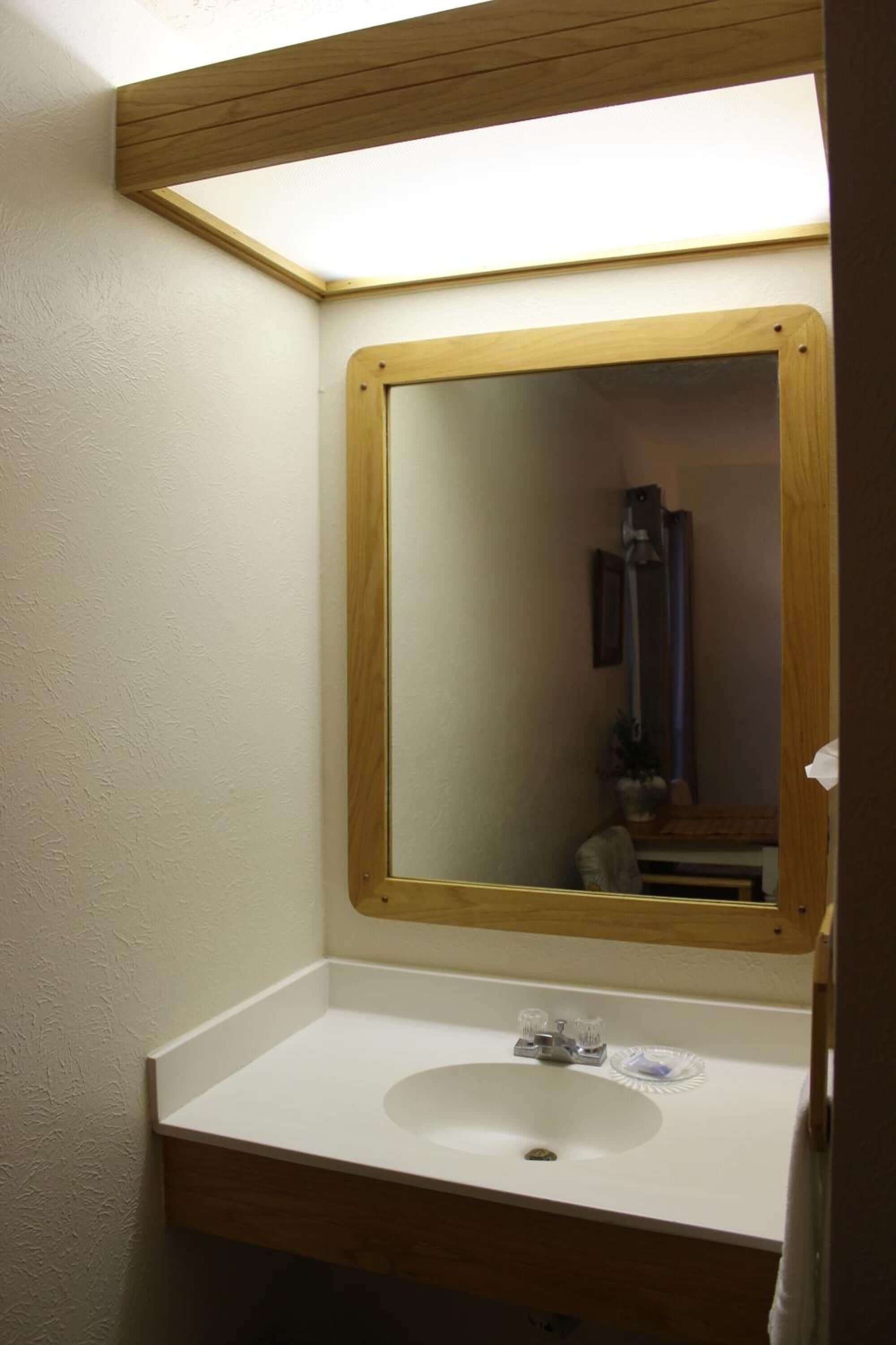 Un baño con espejo de marco de madera, lavabo blanco y una toalla colgada en la puerta.